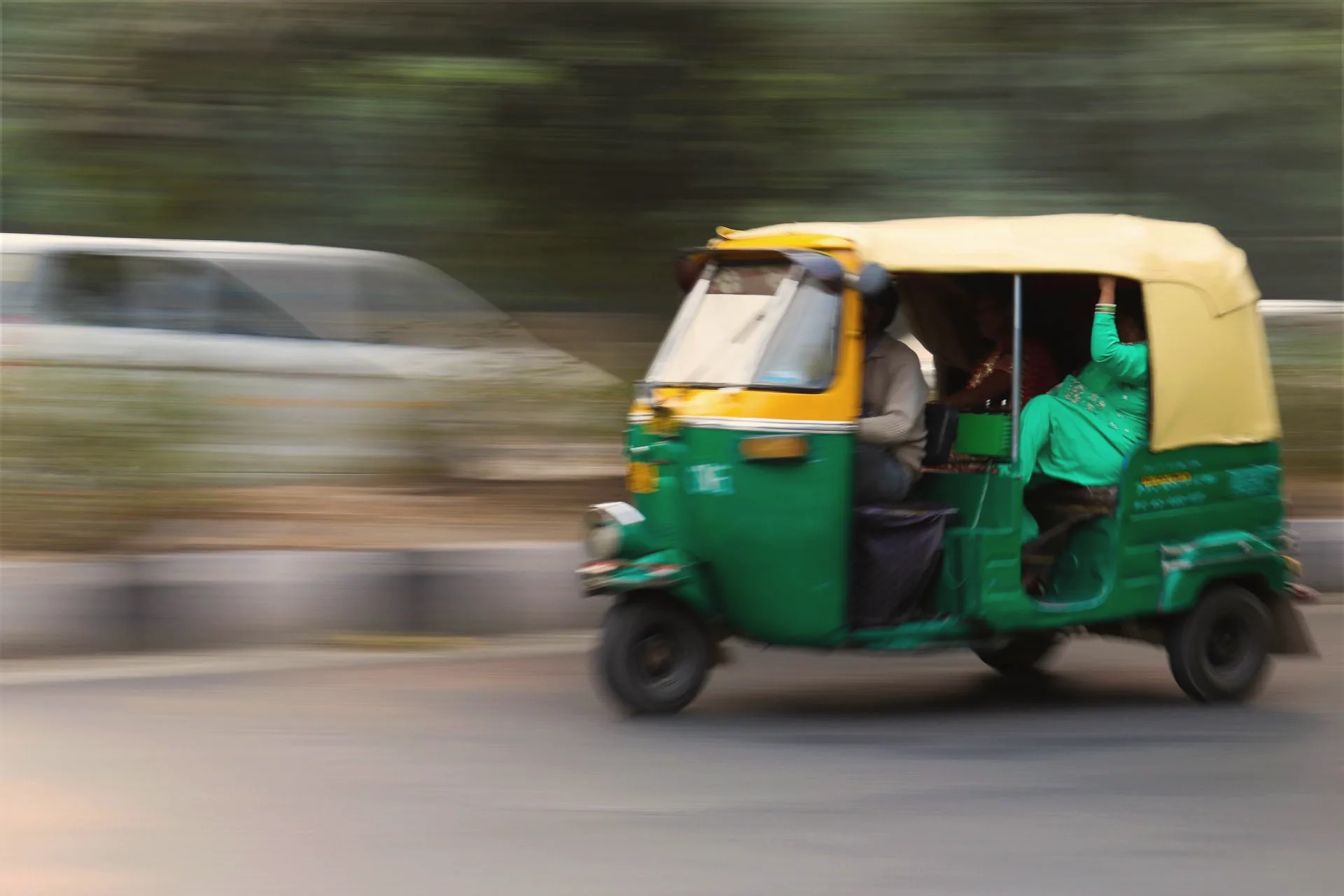 A green and yellow auto rickshaw speeding past, blurred with motion