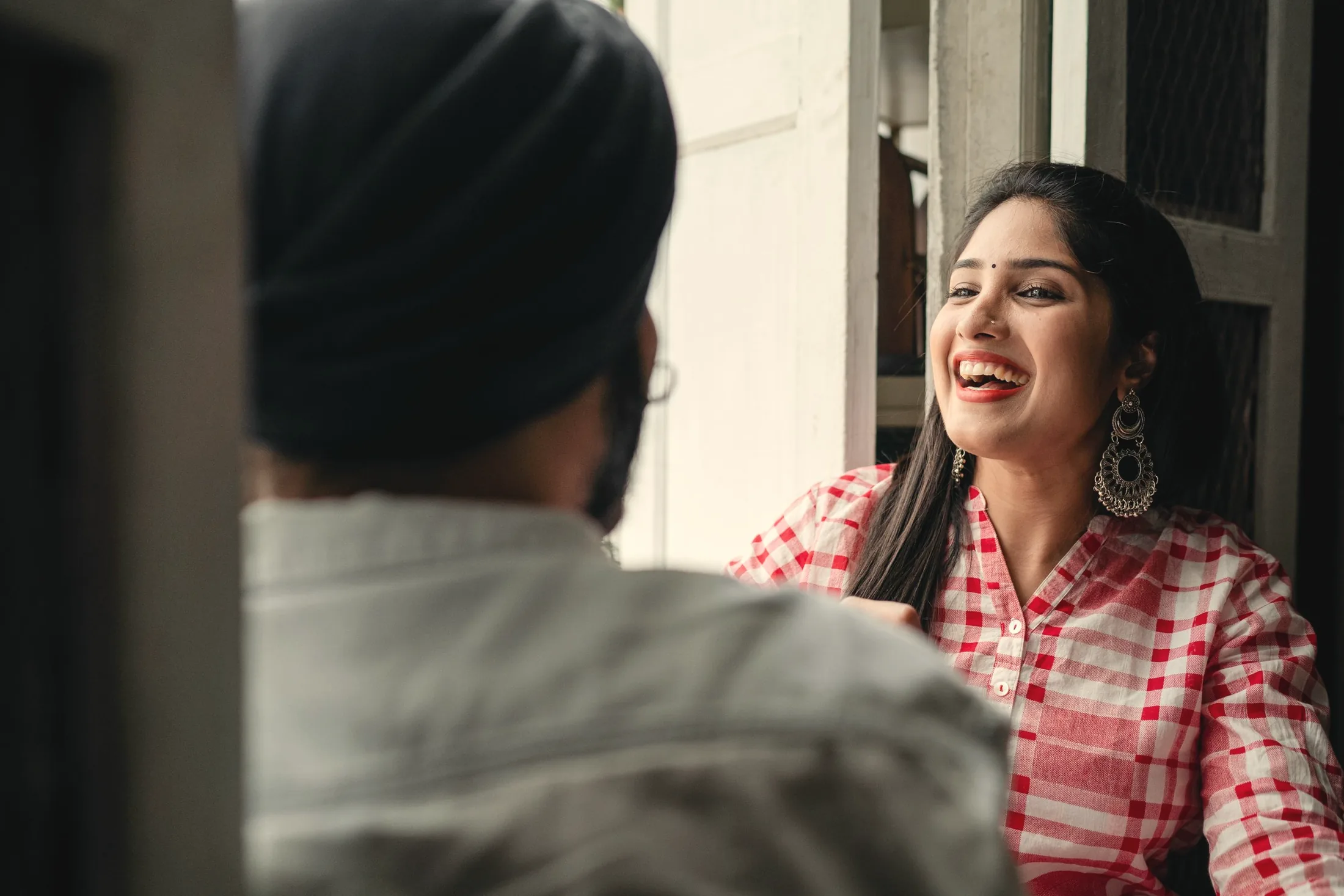 A woman laughing across a café table at the man opposite her, in soft window light