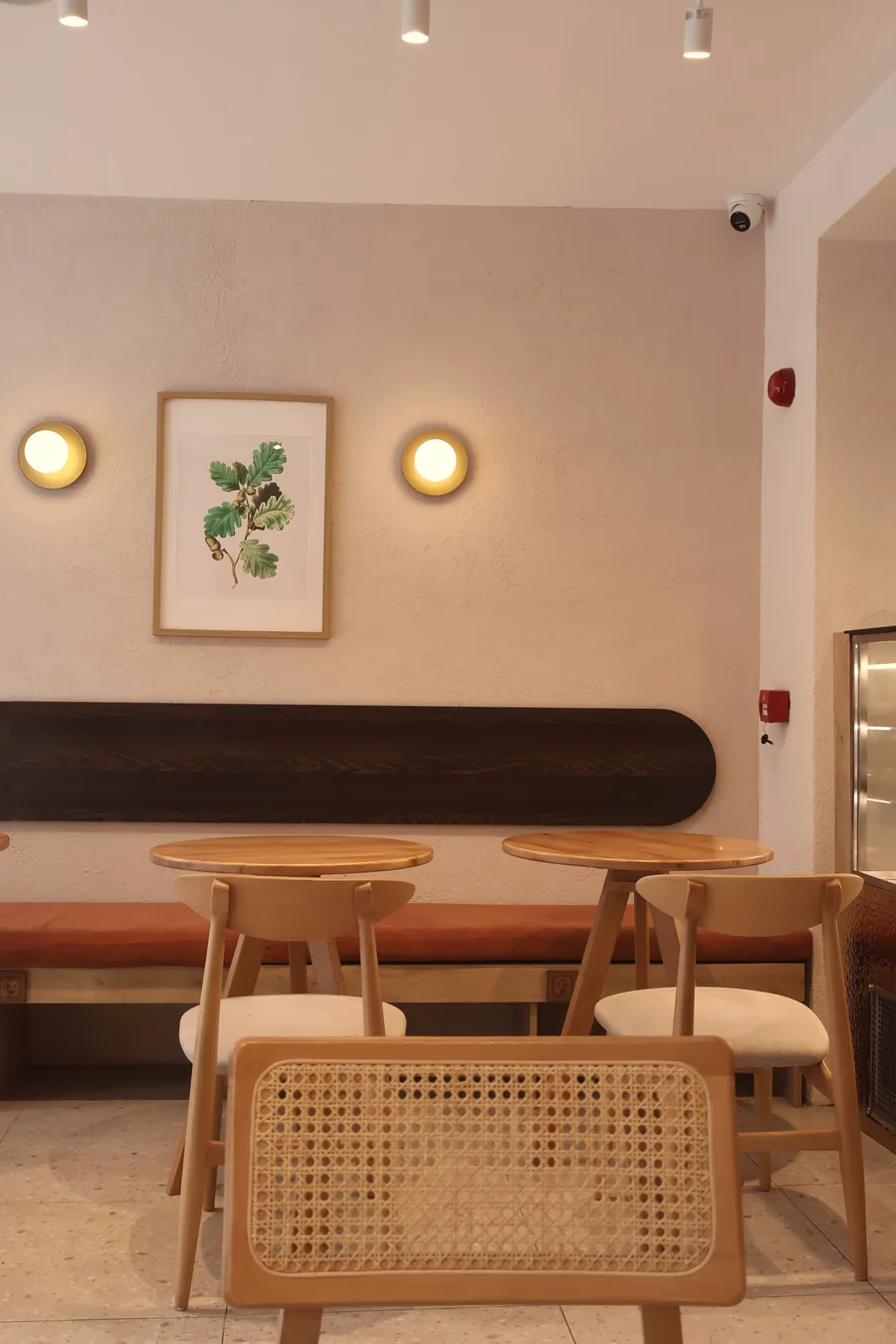 Cane-backed chairs at small round tables in a calm, pale café