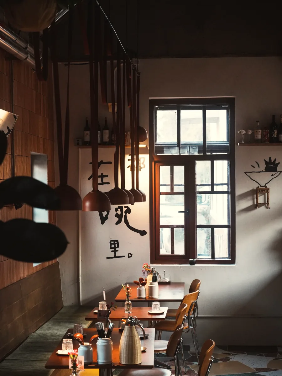 A dim restaurant with pendant lamps over wooden tables set for dinner